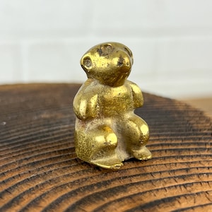 May include: A small, gold-colored, metal figurine of a bear sitting on a wooden surface.