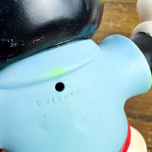 Puede incluir: Una figura vintage de Mickey Mouse, con cabeza negra, torso azul claro y pantalones cortos rojos. La palabra "DISNEY" est&aacute; impresa en la parte posterior. La figura tiene guantes blancos y zapatos amarillos. Un coleccionable cl&aacute;sico de Disney.