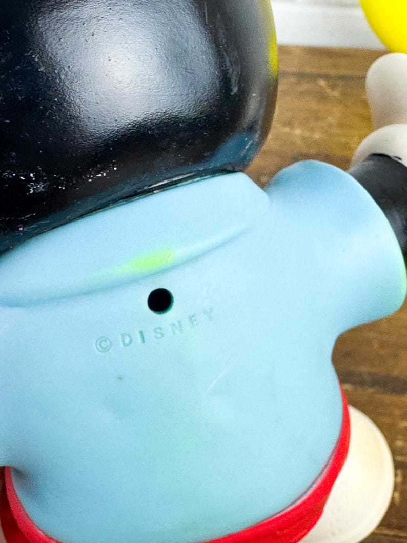 Puede incluir: Una figura vintage de Mickey Mouse, con cabeza negra, torso azul claro y pantalones cortos rojos. La palabra "DISNEY" est&aacute; impresa en la parte posterior. La figura tiene guantes blancos y zapatos amarillos. Un coleccionable cl&aacute;sico de Disney.