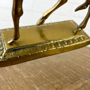 Puede incluir: Una escultura de bronce dorado de un ciervo saltando con una base ornamentada. El ciervo est&aacute; en el aire con las patas extendidas. La base es rectangular con un borde decorativo.