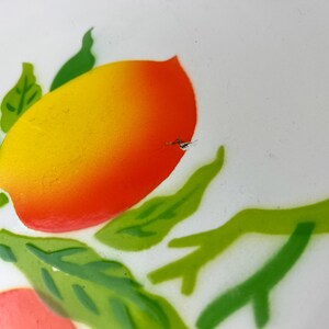 Puede incluir: Un plato de cer&aacute;mica blanco con un dise&ntilde;o pintado de hojas verdes y dos naranjas. Una naranja es amarilla y naranja, y la otra es rosa y naranja.