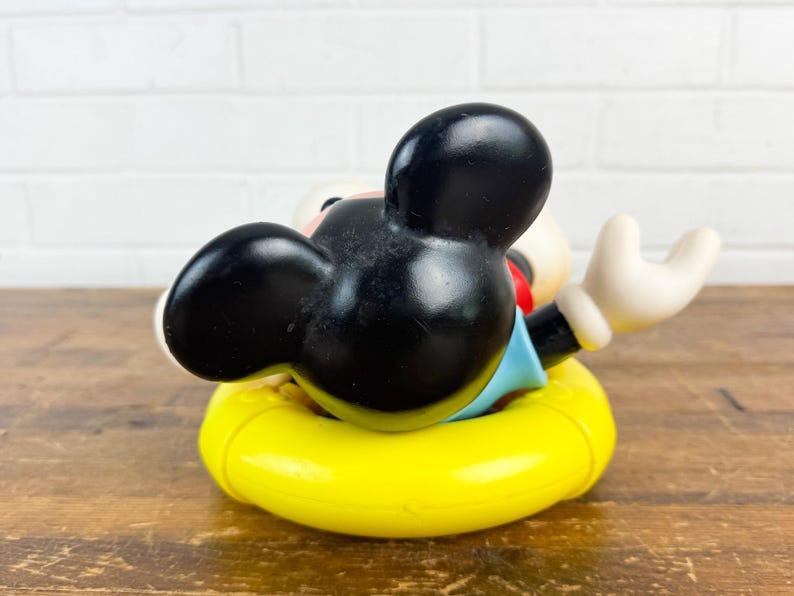 Puede incluir: Figura vintage de Mickey Mouse en un flotador amarillo. El personaje de orejas negras lleva una camisa azul y pantalones cortos rojos. Un objeto de colecci&oacute;n cl&aacute;sico de Disney.