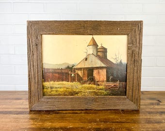 May include: A rustic wooden frame with a vintage print of a small church building with a bell tower. The church is painted in shades of brown and white, with a brown wooden fence in front. The print is set against a background of a field and trees.