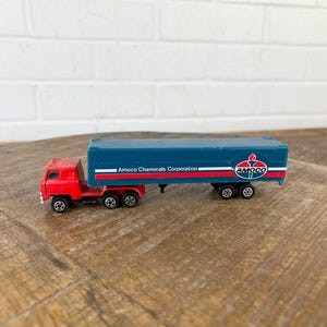 Puede incluir: Un camión de juguete semi-remolque rojo y azul. El remolque tiene las palabras "Amoco Chemicals Corporation" y el logotipo de Amoco en el lateral.
