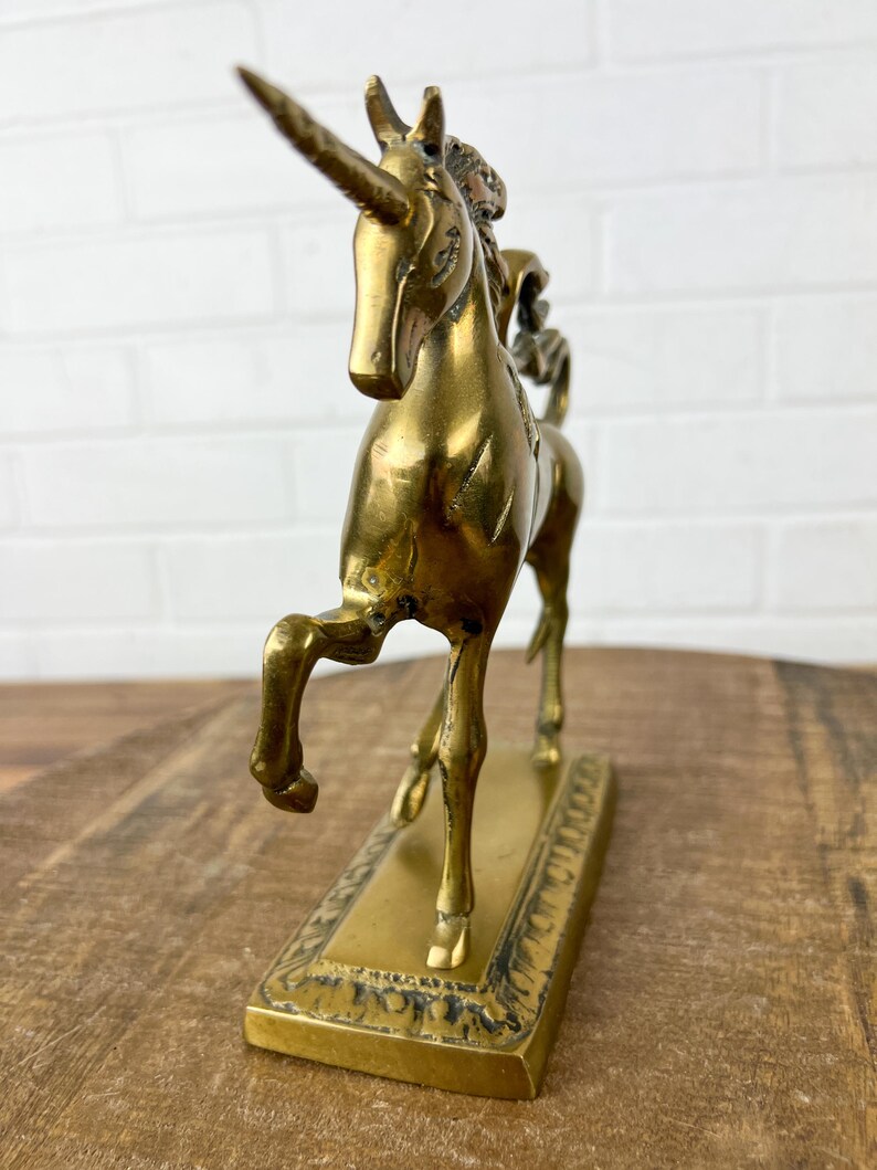 Puede incluir: Una figurita de unicornio de lat&oacute;n dorado con un cuerno y pezu&ntilde;as detalladas. El unicornio est&aacute; de pie sobre una base rectangular con un dise&ntilde;o ornamentado.