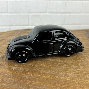 May include: A black glass figurine of a classic Volkswagen Beetle car. The car has a rounded shape and a detailed design.
