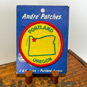 May include: A blue card with the text "Andre' Patches" and a red, green, and yellow embroidered patch depicting the state of Oregon with the text "Portland Oregon".