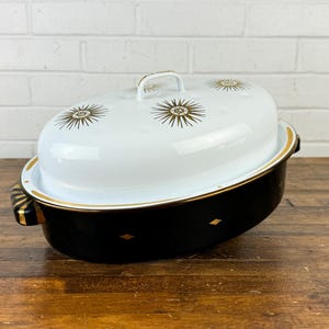 May include: A black and white enamelware casserole dish with a gold rim and gold starburst design. The lid is white with gold starbursts.