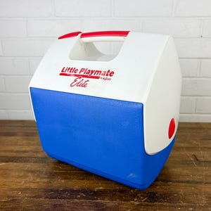 May include: A blue, white, and red Little Playmate Elite cooler by Igloo. The cooler has a white top with a red handle and a blue base. The words "Little Playmate Elite" are printed on the top.