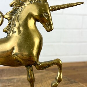 Puede incluir: Una figurita de unicornio de lat&oacute;n dorado con una melena y un cuerno detallados. El unicornio est&aacute; de pie sobre una base con un dise&ntilde;o decorativo.