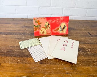 May include: A red box with a floral and figure design, alongside several white cards with Japanese text and two smaller cards. The box features illustrations of children and flowers.