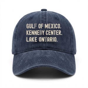 Könnte beinhalten: Eine marineblaue Baseballkappe mit verwaschener Optik. Auf der Vorderseite befindet sich eine hellcremefarbene Stickerei mit dem Text: GULF OF MEXICO. KENNEDY CENTER. LAKE ONTARIO. Die Kappe hat eine strukturierte Krone und einen gebogenen Schirm.