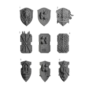 May include: A collection of six grey miniature shields featuring intricate relief designs including a lion head, skulls, a sword, and religious figures. Each shield is numbered and displays detailed textures, rivets, and mounting brackets on the reverse side.