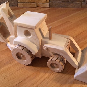 May include: A wooden toy backhoe loader, crafted from light-colored wood. The toy features a detailed design with a front bucket, rear arm, and large wooden wheels. The backhoe is designed to resemble a real construction vehicle.