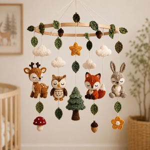 May include: A circular wooden mobile featuring crocheted woodland elements including a deer, owl, fox, and rabbit. The mobile is decorated with crocheted clouds, green leaves, a yellow star, a pine tree, a red mushroom, an acorn, and a yellow flower.