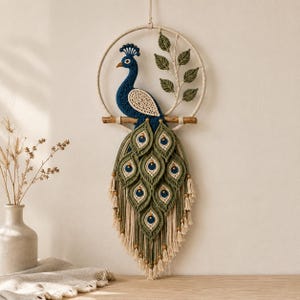 Op de afbeelding: Een macramé wandhanger met een donkerblauwe pauw met een crèmekleurige vleugel, zittend op een houten tak in een cirkelvormig frame. De pauw heeft een lange, uitgebreide staart gemaakt van olijfgroen en crème geknoopt koord met blauwe accenten.