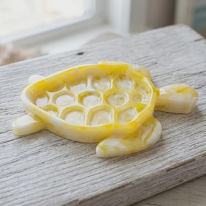 May include: A turtle-shaped trinket dish crafted from a marbled resin material featuring a blend of translucent yellow and opaque white colors. The shell section of the dish has a raised, segmented pattern with a smooth, glossy finish throughout.