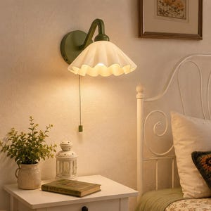 May include: A wall-mounted lamp featuring a matte olive green circular base and an angled arm supporting a white, scalloped, fluted glass shade. The fixture includes a vertical pull chain with a small green cylindrical handle for operation.