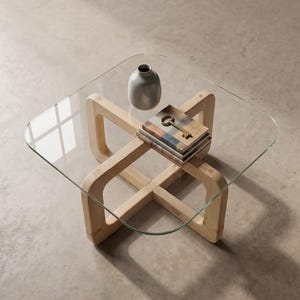 Pode incluir: Uma mesa de centro quadrada com tampo de vidro transparente e base de madeira clara com design em cruz. Sobre a superfície de vidro encontram-se um pequeno vaso de cerâmica cinzenta e uma pilha de dois livros com uma chave de metal antiga.