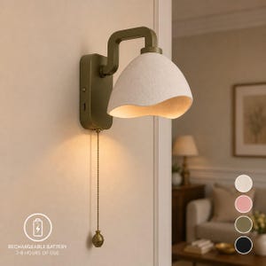 May include: A wall-mounted lamp with a matte olive green metal base and a curved arm. The lamp features a textured, off-white, bell-shaped shade with a wavy bottom edge. A thin metal pull chain with a small spherical weight hangs from the base.