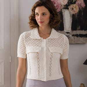 May include: A short-sleeved, cream-colored knit cardigan featuring a collared neckline, a button-down front, and two decorative chest pockets. The garment is crafted with a delicate, open-work lace pattern throughout the bodice and sleeves.