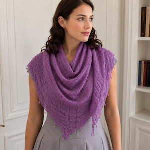 May include: A triangular purple knit shawl featuring an intricate openwork lace pattern and small bead accents along the edges. The shawl is draped over the shoulders, showcasing a delicate texture and a pointed hemline that falls toward the waist.