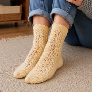 Peut inclure: Une paire de chaussettes en tricot jaune pâle présentant un délicat motif de feuilles en dentelle verticale sur le devant. Les chaussettes ont un bord-côte festonné en haut et une texture en tricot lisse et unie au niveau du talon et des orteils.
