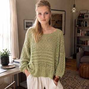 May include: A light green, loose-fitting knit sweater featuring a wide scoop neckline, long sleeves with ribbed cuffs, and a complex openwork pattern that alternates between diamond-shaped mesh sections and horizontal bands of solid knit stitches.