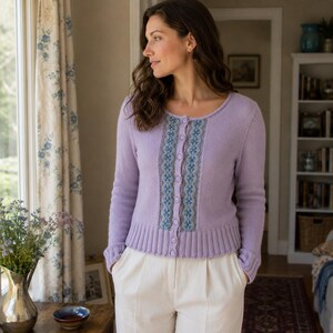 May include: A light purple long-sleeve cardigan featuring a central vertical panel with a blue and white floral pattern, a round neckline, and a button-down front closure. The garment has ribbed cuffs and a ribbed hem, paired with white trousers.