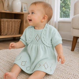 May include: A light mint green knitted dress and matching bolero set. The dress features a diamond-shaped openwork pattern along the hem and a single diamond cutout at the chest. The bolero has short sleeves and a decorative bobble trim edge.