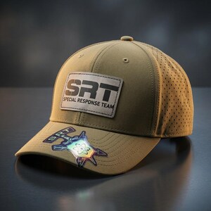May include: A tan baseball cap with a perforated side panel and a rectangular patch on the front featuring the black text SRT SPECIAL RESPONSE TEAM. A holographic sticker with an atom symbol and the text SRT is attached to the curved brim.