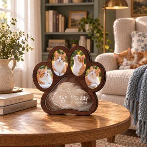 May include: A dark wood paw-shaped pet memorial frame featuring four oval photo slots containing images of an orange and white cat. The large bottom section includes a white line drawing of a dog and the text Teddy 10/03/2018 etched on glass.
