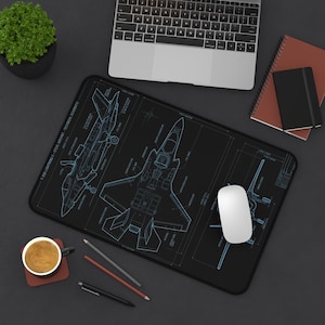 Peut inclure: Un tapis de bureau rectangulaire noir présentant un schéma technique bleu d'un avion F-35B Lightning II. Le design comprend des dessins au trait détaillés de l'avion sous plusieurs angles avec des étiquettes, sur une surface sombre.