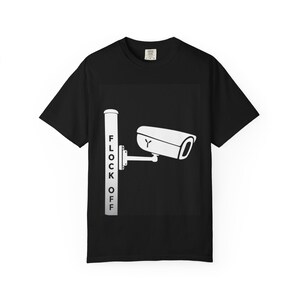Peut inclure: Un t-shirt noir à manches courtes avec un motif blanc représentant une caméra de surveillance montée sur un poteau. Le poteau porte l'inscription FLOCK OFF imprimée verticalement en lettres capitales noires. Col rond classique.