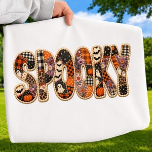 May include: A white t-shirt featuring the word SPOOKY in large, block letters. Each letter is filled with a patchwork design of various patterns including pumpkins, ghosts, bats, plaid, leopard print, and floral motifs with a stitched border.