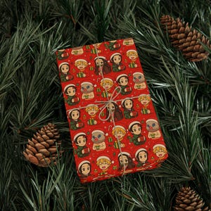 Puede incluir: Una caja de regalo rectangular envuelta en papel rojo con un patrón repetitivo de personajes de anime con gorros de Papá Noel sosteniendo regalos, atada con un cordel fino de color canela, sobre agujas de pino verdes y piñas.