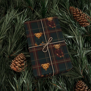 Puede incluir: Una caja de regalo rectangular envuelta en papel de cuadros verde oscuro y rojo con un patrón repetitivo de osos de peluche marrones en pijama, atada con un cordel beige fino que forma un lazo en el centro del paquete.