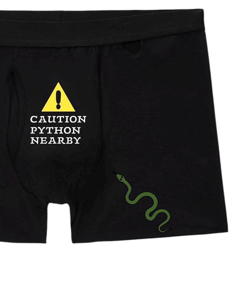 Peut inclure: Cale&ccedil;on noir avec un panneau d'avertissement triangulaire jaune portant un point d'exclamation et le texte CAUTION PYTHON NEARBY en lettres capitales blanches. Une petite illustration de serpent vert est situ&eacute;e sous le texte.