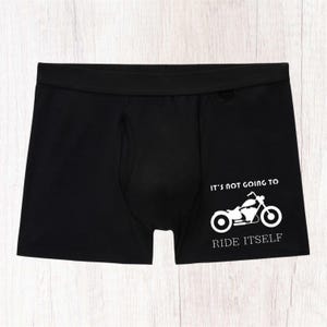 May include: Black boxer briefs featuring a white graphic of a motorcycle on the right side. The text above the motorcycle reads IT'S NOT GOING TO and the text below the motorcycle reads RIDE ITSELF in a clean, white, sans-serif font.