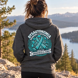 Op de afbeelding: Een donker antracietgrijze hoodie met een turquoise bewustwordingslint op de achterkant. Het ontwerp bevat de tekst Dysautonomia Warriors & Supporters United for Awareness & Cure, omringd door diverse anatomische iconen.