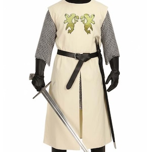 May include: A medieval-style costume featuring a cream-colored sleeveless tunic with two gold lion emblems on the chest, worn over a chainmail-patterned long-sleeve shirt. The outfit includes a black belt, black gloves, black boots, and a metal sword.