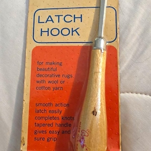 May include: A Boye brand latch hook tool with a light wood handle and a metal hook, packaged on a vintage cardboard backing card. The card features orange and blue graphics with text including LATCH HOOK, ITEM 7430, and THE BOYE NEEDLE COMPANY.