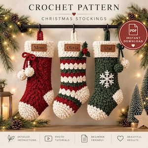 Op de afbeelding: Drie gehaakte kerstsokken hangen aan een zwarte roede. De linker is rood met witte rand en pompons, de middelste is rood, wit en groen gestreept met hulst, en de rechter is groen met een witte sneeuwvlok en pompons.