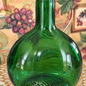 May include: A round, emerald green glass bottle with a narrow, cylindrical neck and a thick, reinforced rim. The glass is smooth and translucent, featuring a bulbous, spherical body that tapers upwards into a slender neck design.