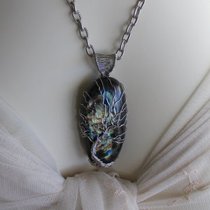 May include: A silver chain necklace with a pendant featuring a dark blue and green gemstone wrapped in silver wire, resembling a tree.