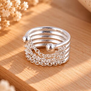 May include: A silver ring featuring five stacked bands connected by delicate silver chains. The ring has two small silver spheres at the open ends and is stamped with the text S925 on the interior surface of the top band.