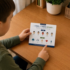 Può includere: Una tavola di comunicazione rettangolare bianca intitolata I FEEL / I NEED BOARD con due file di icone colorate. La riga superiore mostra cinque espressioni facciali etichettate come happy, sad, angry, worried e scared. La riga inferiore mostra icone per break, quiet, help, hug e space.