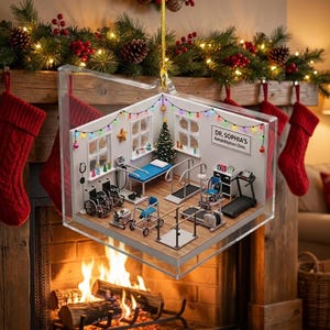 May include: A clear, multi-faceted hanging ornament containing a miniature rehabilitation clinic scene. The interior features a Christmas tree, medical equipment, wheelchairs, and a sign reading DR. SOPHIA'S Rehabilitation Clinic.