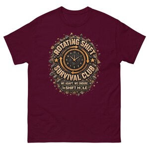 May include: A maroon short-sleeve t-shirt featuring a central graphic of a clock surrounded by rocks and the text "ROTATING SHIFT SURVIVAL CLUB," "WE ADAPT. WE ENDURE.," and "THE SHIFT HOLE" in tan and black lettering with circular arrows.