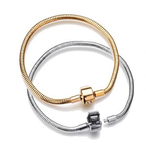 May include: Two snake chain bracelets, one in a gold tone and one in a silver tone. Each bracelet features a cylindrical barrel clasp mechanism. The gold bracelet is closed, while the silver bracelet is shown with its clasp open, revealing the internal pin.